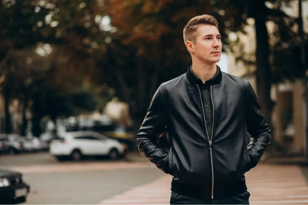 "Man in a black leather bomber jacket walking through an autumn urban environment, perfect for fall styling."
