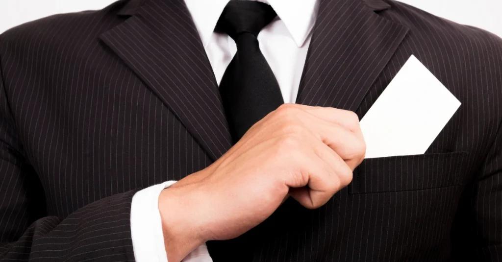 Businessman in a pinstripe suit putting a white business card in the breast pocket.