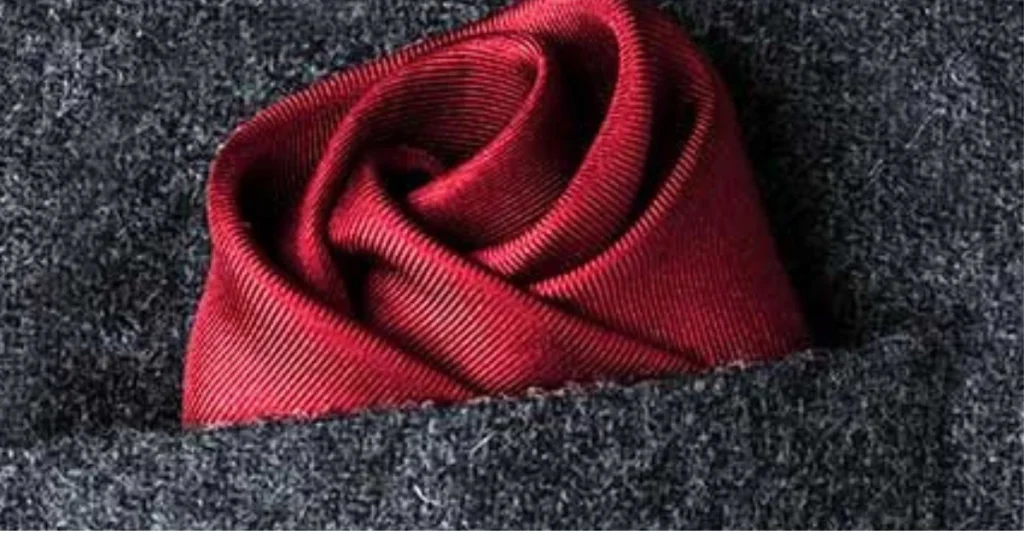 Close-up of a red silk pocket square folded into a rose shape, nestled in a grey suit pocket.