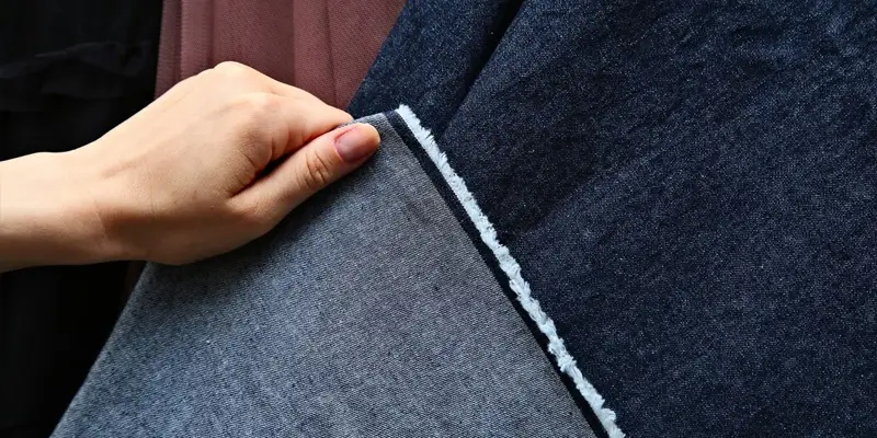 "Hand holding denim fabric with frayed edges, demonstrating denim texture for pant guide blog."