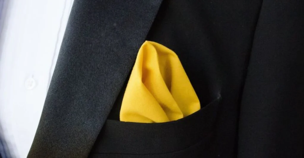 Close-up of a yellow pocket square neatly folded in the breast pocket of a black suit jacket.