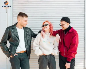 A group of three friends, one in a leather jacket, one in a white sweater, and one in a red jacket, laughing and wearing trendy activewear in front of a white background used to show difference between jacket and sweater