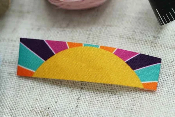 colorful sublimated patch of a sun with vibrant rays in pink, turquoise, and orange on fabric.