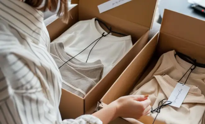 A person sorting packaged clothing items in shipping boxes, preparing for delivery with price tags attached.