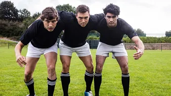 three rughy palyer standing in a defence form wearing black t shirt and white shorts