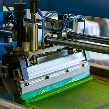 Close-up of a screen printing press applying green ink to a mesh screen, a key step in textile printing for vibrant designs.