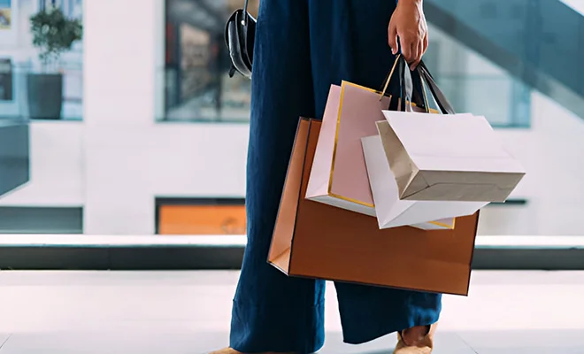 A person holding multiple shopping bags from different stores while walking through a shopping mall.