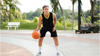 Basketball player in black and yellow uniform dribbling a ball on an outdoor court.