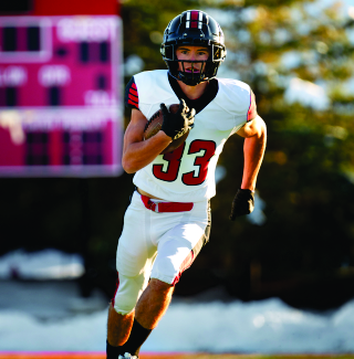 A football player in a white uniform with the number 33 running with the ball during a game on an outdoor field.