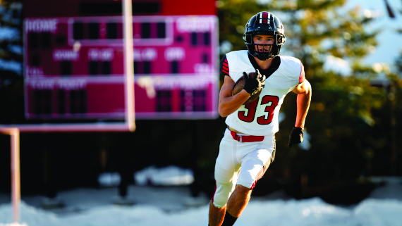 A football player in a white uniform with the number 33 running with the ball during a game on an outdoor field