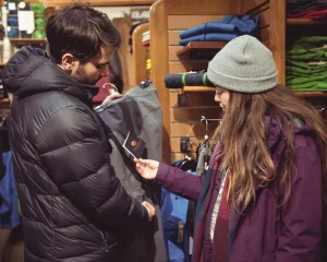 Customers shopping for winter clothing in a retail store, examining a jacket with a private label tag, highlighting quality and brand focus in the fashion industry.